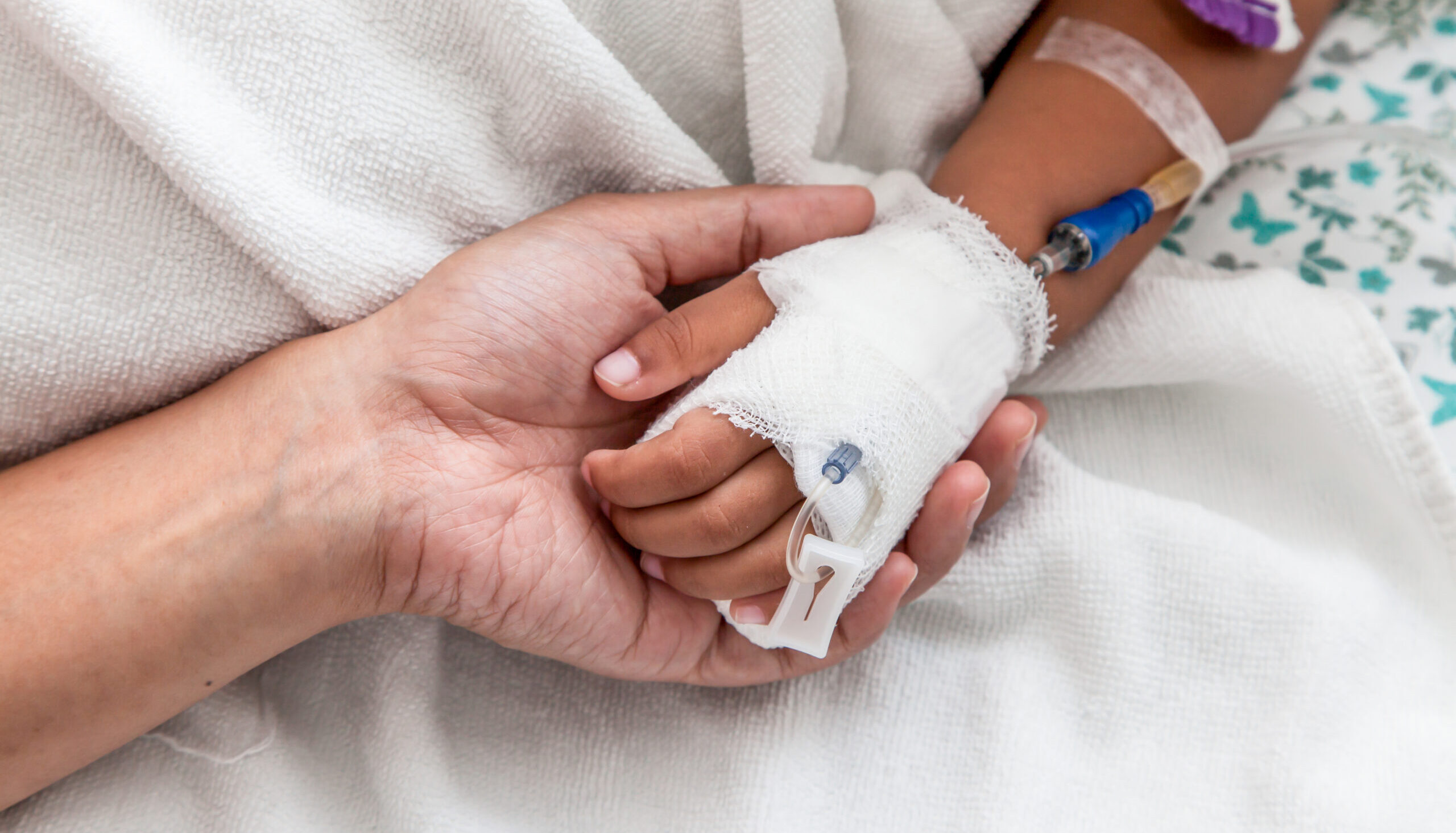 mother holding child's hand who have IV solution in the hospital