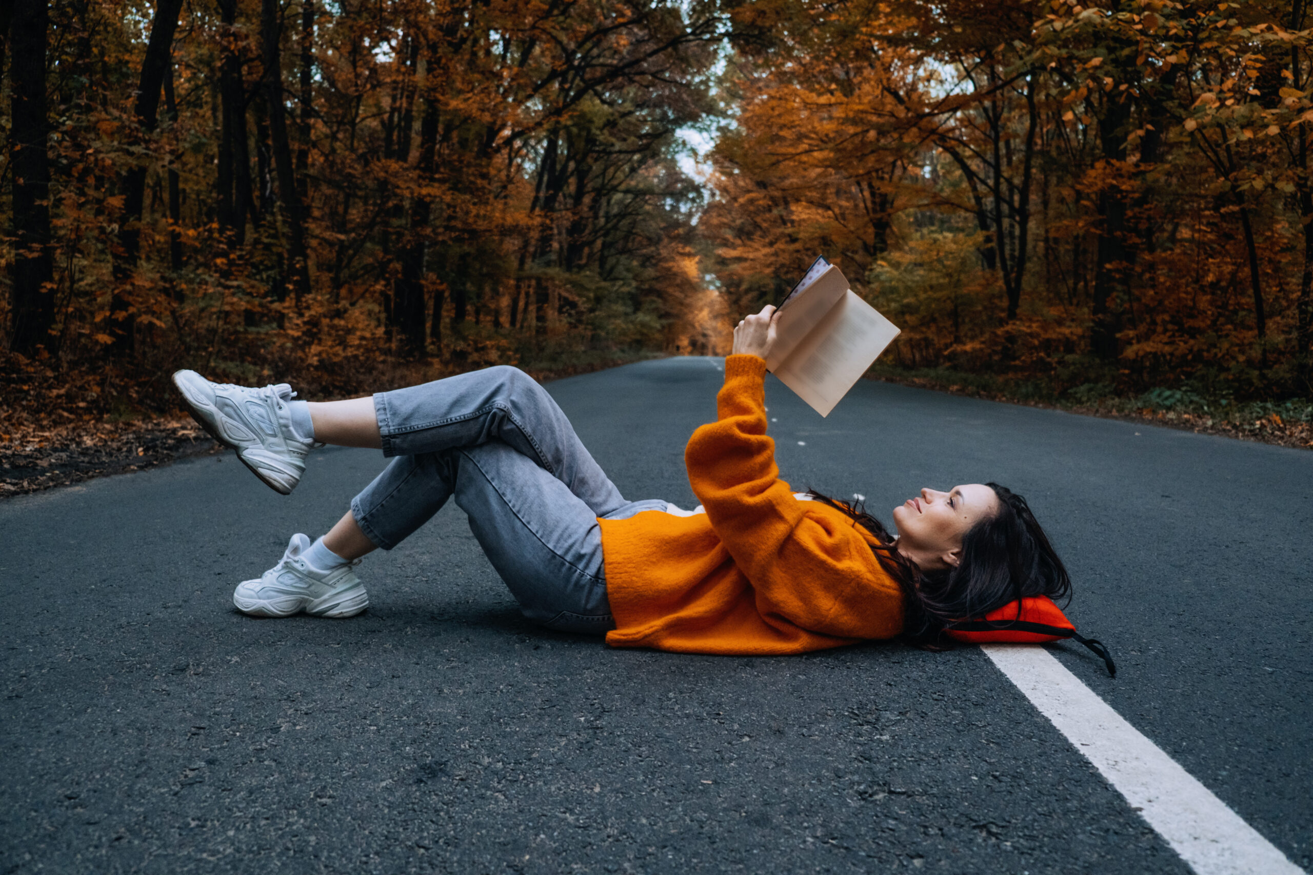 Confidence woman with book sitting on the road with autumn tree around. New life, path choice, ambition, right direction concept