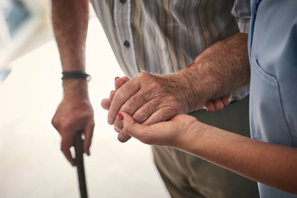 Female nurse supporting senior man to walk. Focus on hands.