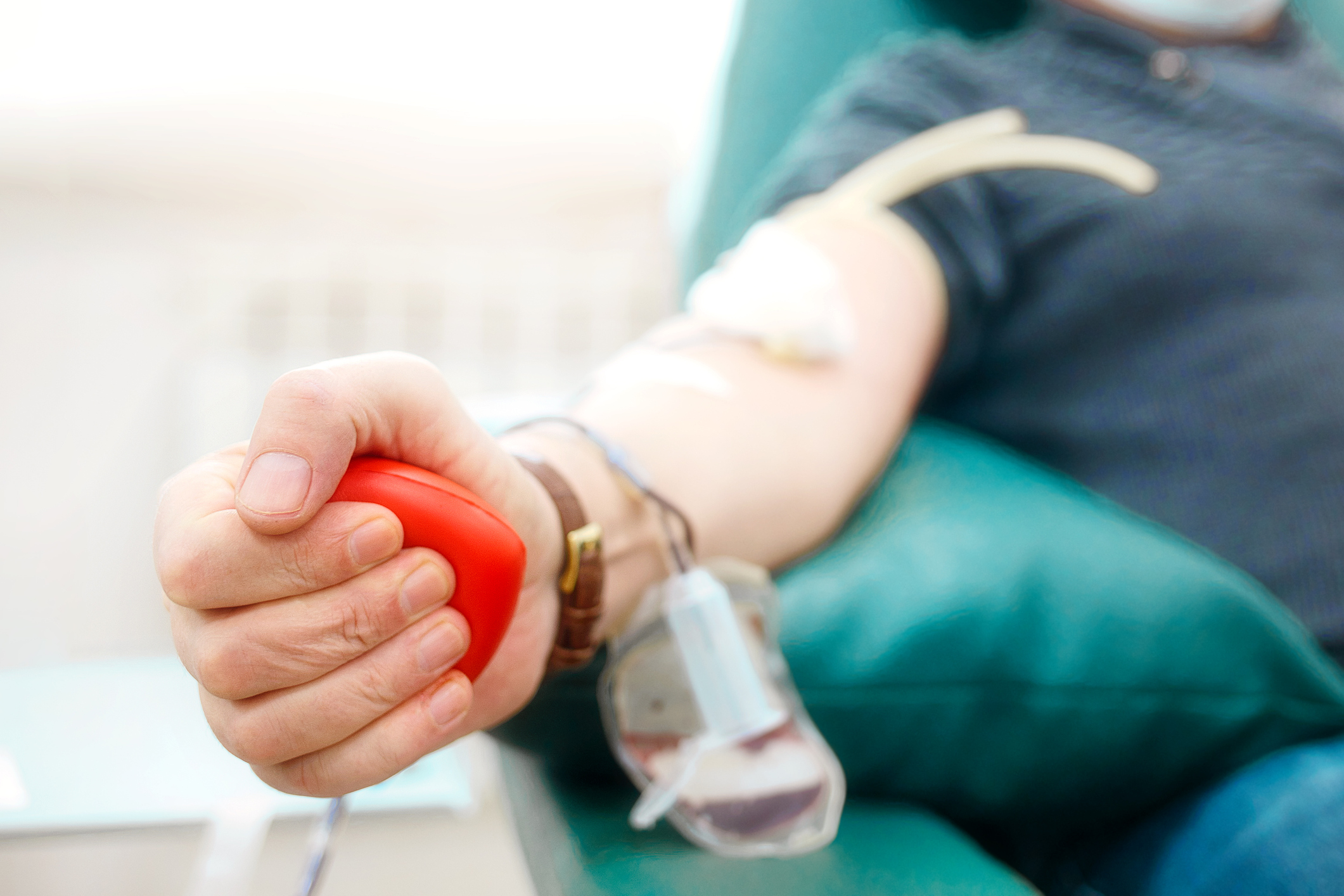 Topic of donation. Man donates blood in hospital. Man's hand squeezes rubber heart. Close-up. Donor sits in chair. Background.