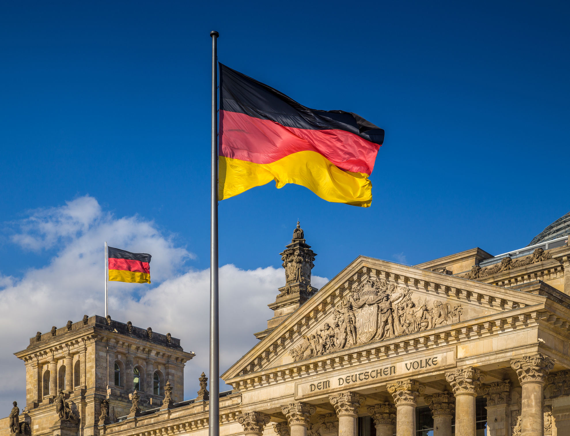 German flags waving in the wind at famous Reichstag building, seat of the German Parliament (Deutscher Bundestag), on a sunny day with blue sky and clouds, central Berlin Mitte district, Germany.