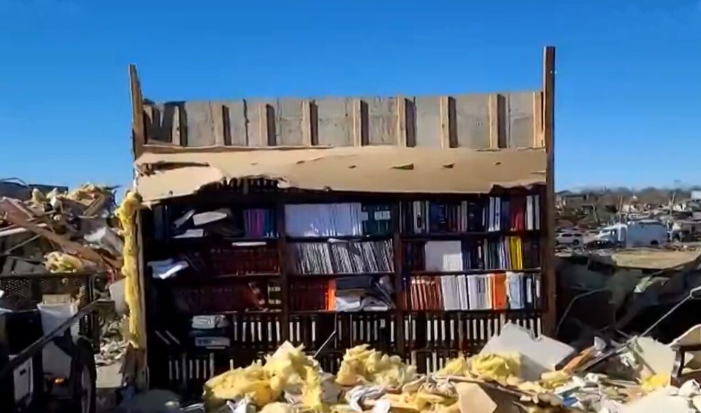 Imagem Ilustrando a Notícia: Estante de livros permanece intacta em meio à destruição causada por tornados, no sudeste dos EUA
