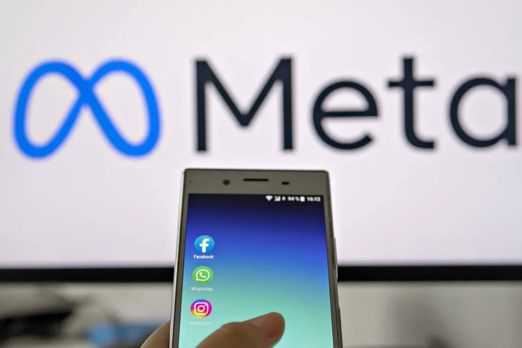 Smartphone display with logo of Facebook, WhatsApp and Instagram apps in hand against blurred META logotype on white monitor background: Tallinn, Estonia - October 29, 2021