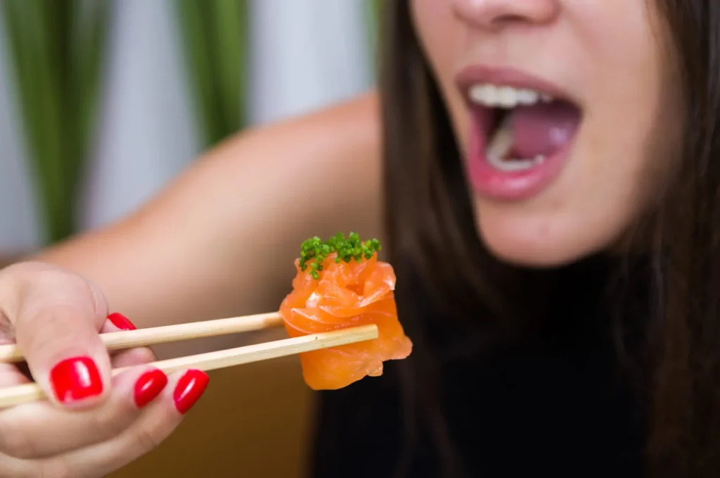 Woman eating delicious gunkan sushi, closeup on chopsticks