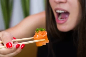 Woman eating delicious gunkan sushi, closeup on chopsticks