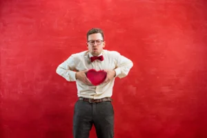 Young beautiful man with abstract heart on red studio background
