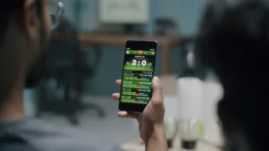 Unrecognizable fans with smartphones discussing online stakes and watching football competition on TV at home