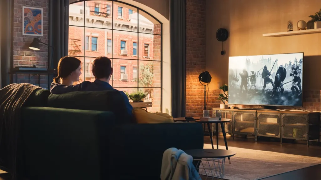 Authentic Couple Spending Time at Home, Sitting on a Couch and Watching Latest Blockbuster on Flat Screen Television Set. Man and Woman Streaming Movie or Show Using Home Cinema System.
