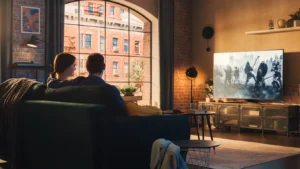 Authentic Couple Spending Time at Home, Sitting on a Couch and Watching Latest Blockbuster on Flat Screen Television Set. Man and Woman Streaming Movie or Show Using Home Cinema System.