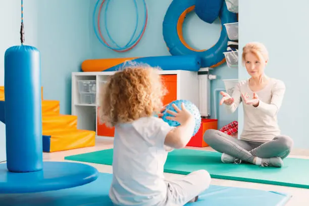 Boy playing with his therapist using a ball