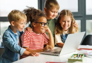 Positive kids pupils  schoolchildren    happy smiling, sitting at desk and   looking at laptop screen during online lesson