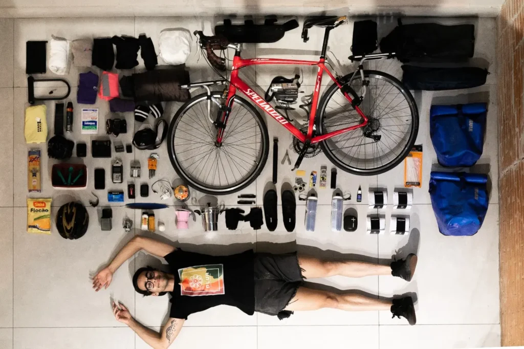 Pedro Paulo Medrado, 23, deitado no chão ao lado de sua bicicleta e demais itens que usa para a viagem | Foto: Divulgação
