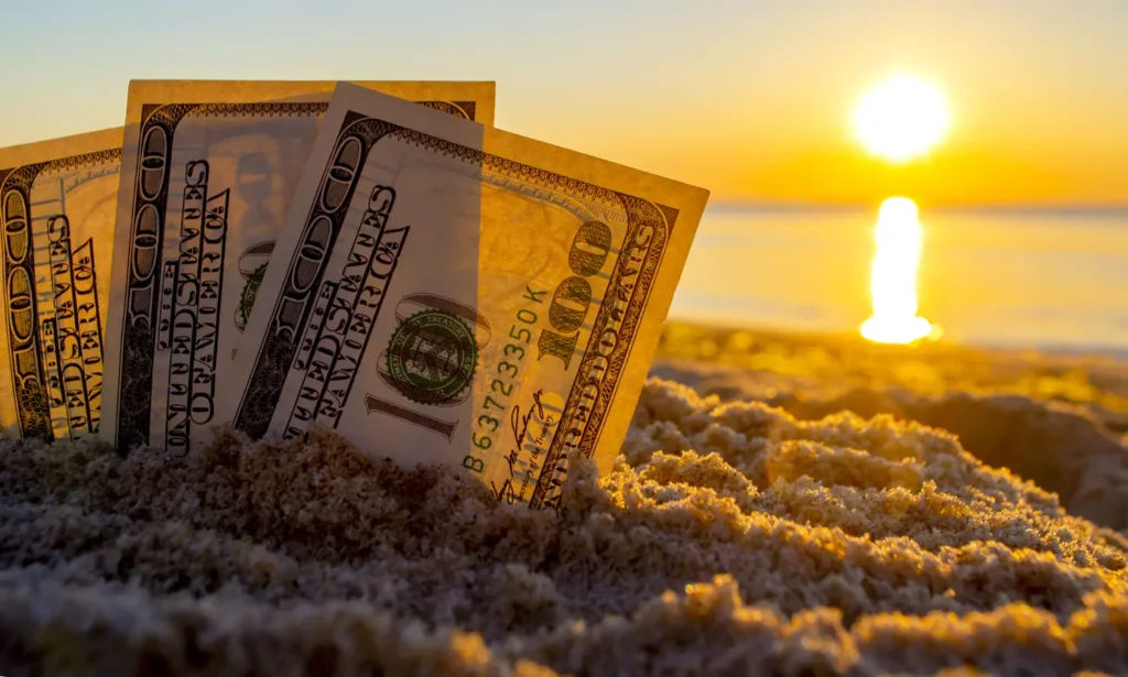 Three dollar bills are buried in sand on sandy beach near sea at sunset dawn in summer close-up. Money. Dollars covered sand. Money grows in ground. Finance and investment concept.