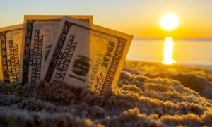 Three dollar bills are buried in sand on sandy beach near sea at sunset dawn in summer close-up. Money. Dollars covered sand. Money grows in ground. Finance and investment concept.