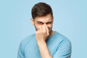 Young man holding his nose as if smelling something rotten and stinky, trying to find source of odor