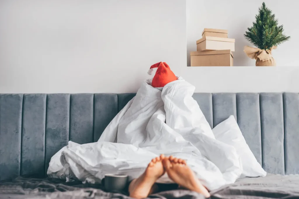 Wake up morning after party holidays. Woman in Santa hat under blanket in bed.