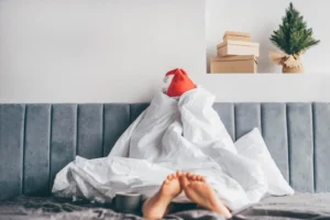 Wake up morning after party holidays. Woman in Santa hat under blanket in bed.