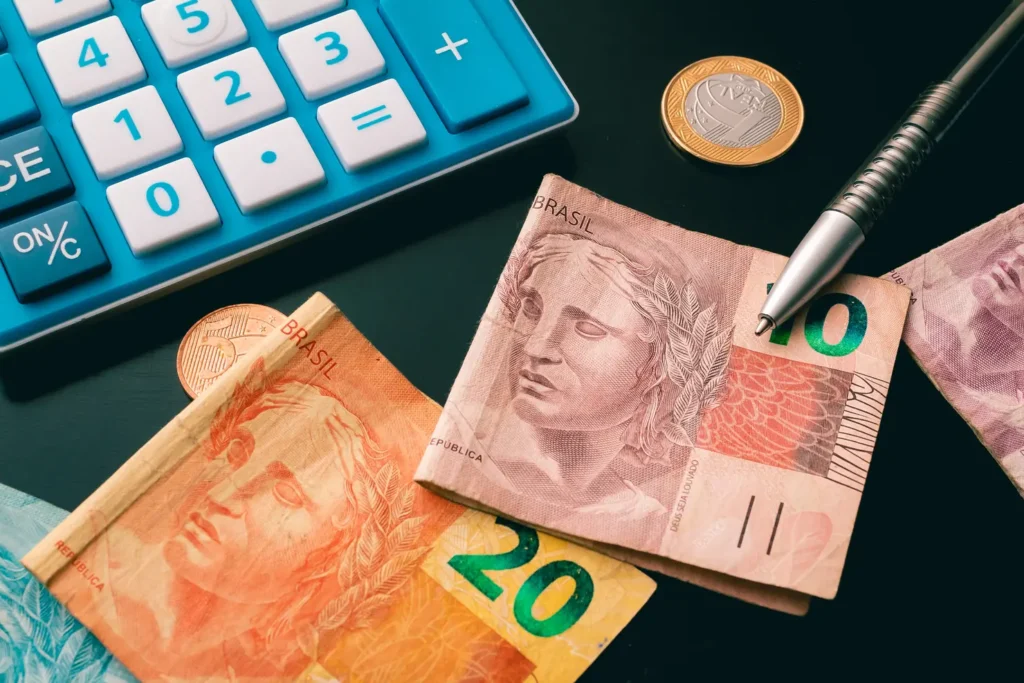 Real currency, money from Brazil. Some Brazilian Real banknotes on a dark table with a calculator, pen and some coins for Brazilian economy, finance and investment concept.