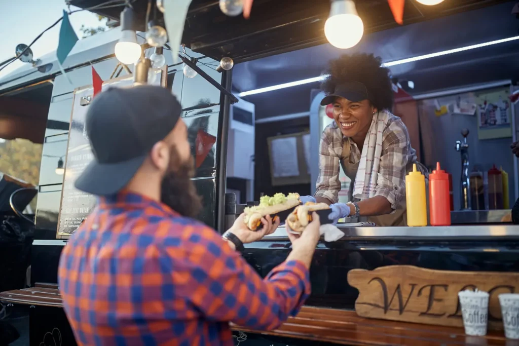 polite afro-american female employee holding, giving, two sandwiches to a satisfied beardy caucasian customer. fast food service