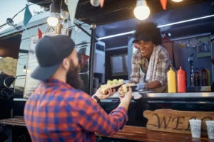 polite afro-american female employee holding, giving, two sandwiches to a satisfied beardy caucasian customer. fast food service