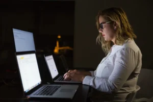 Businesswoman using laptop in dark office. Side view of professional young businesswoman working with laptop computer late at night. Business and technology concept