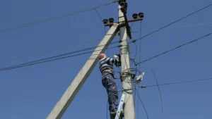 Electricity work, man repairs electric pole wearing all the safety equipment, climbing with a stair