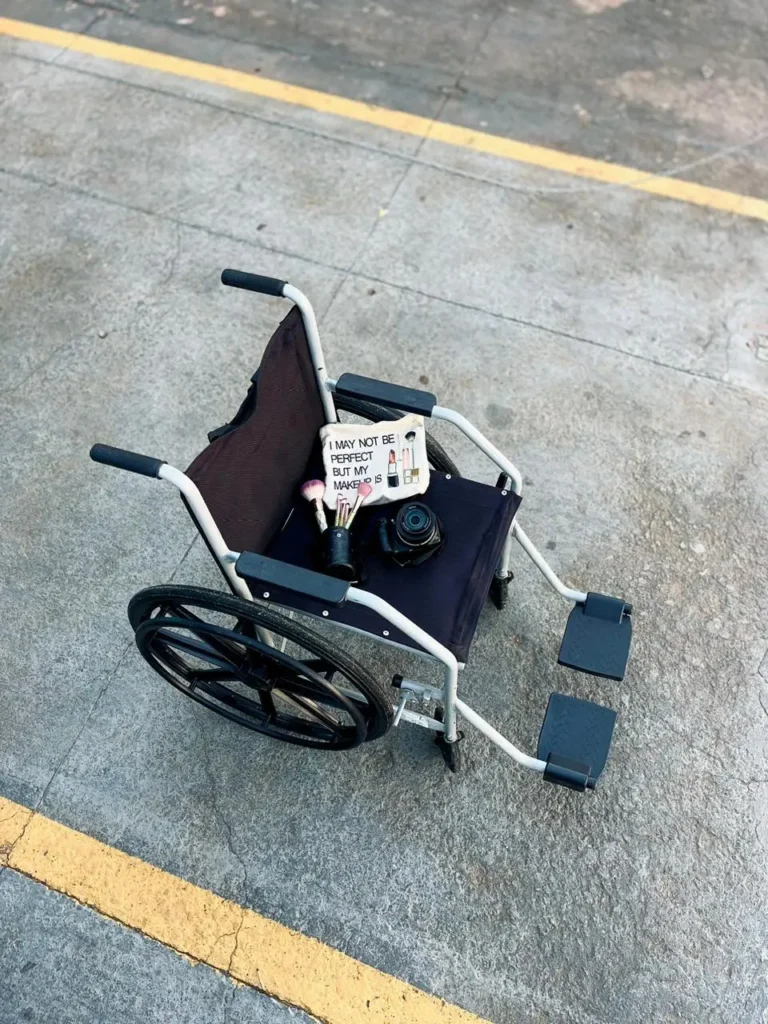 Para todos verem: uma cadeira de rodas com uma nécessaire que traz a frase 'Posso não ser perfeita, mas minha maquiagem é', acompanhada de pincéis de maquiagem e uma câmera Foto: Vitória Sousa de Oliveira